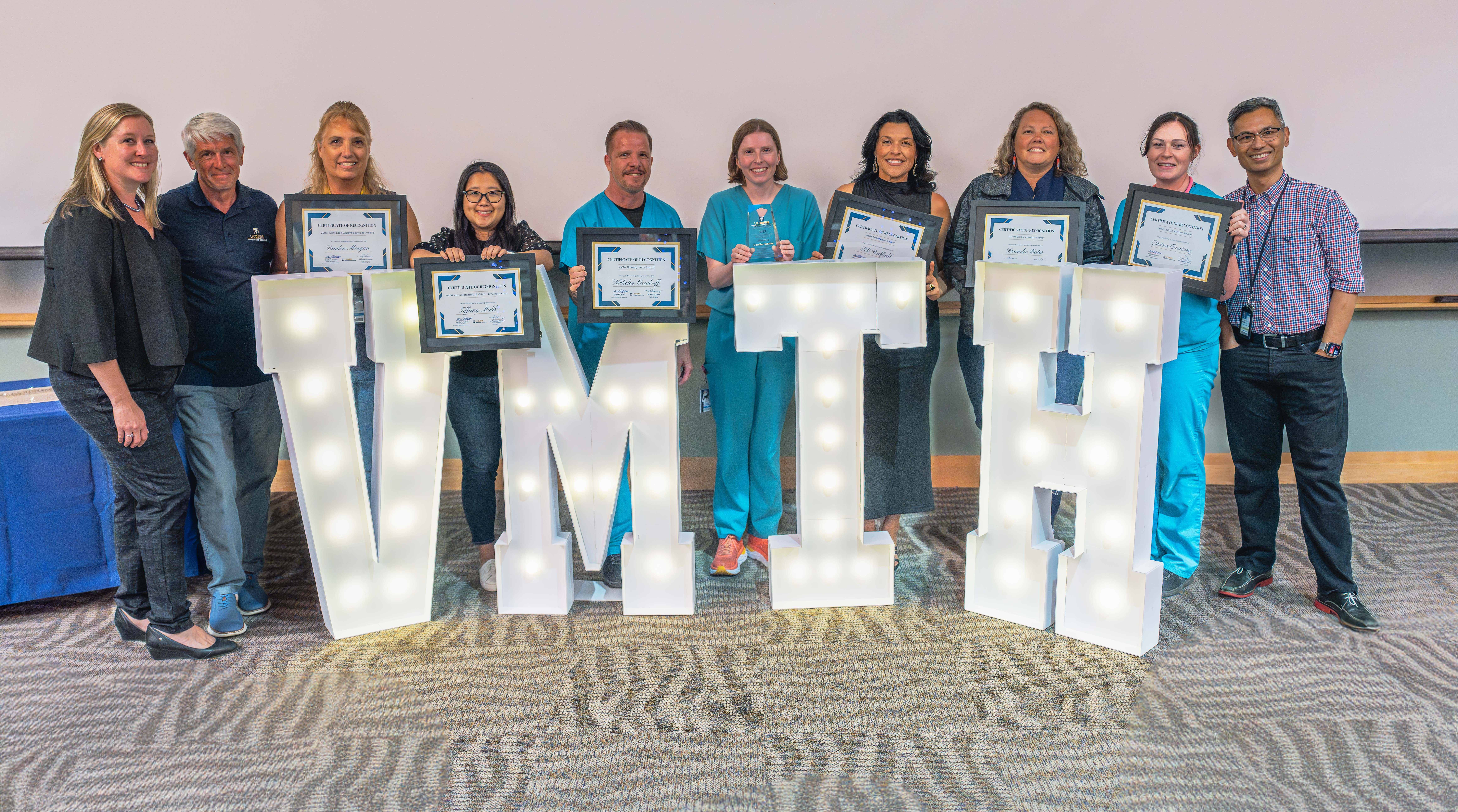 group of award winners standing behind giant light boxes shaped as letters VMTH