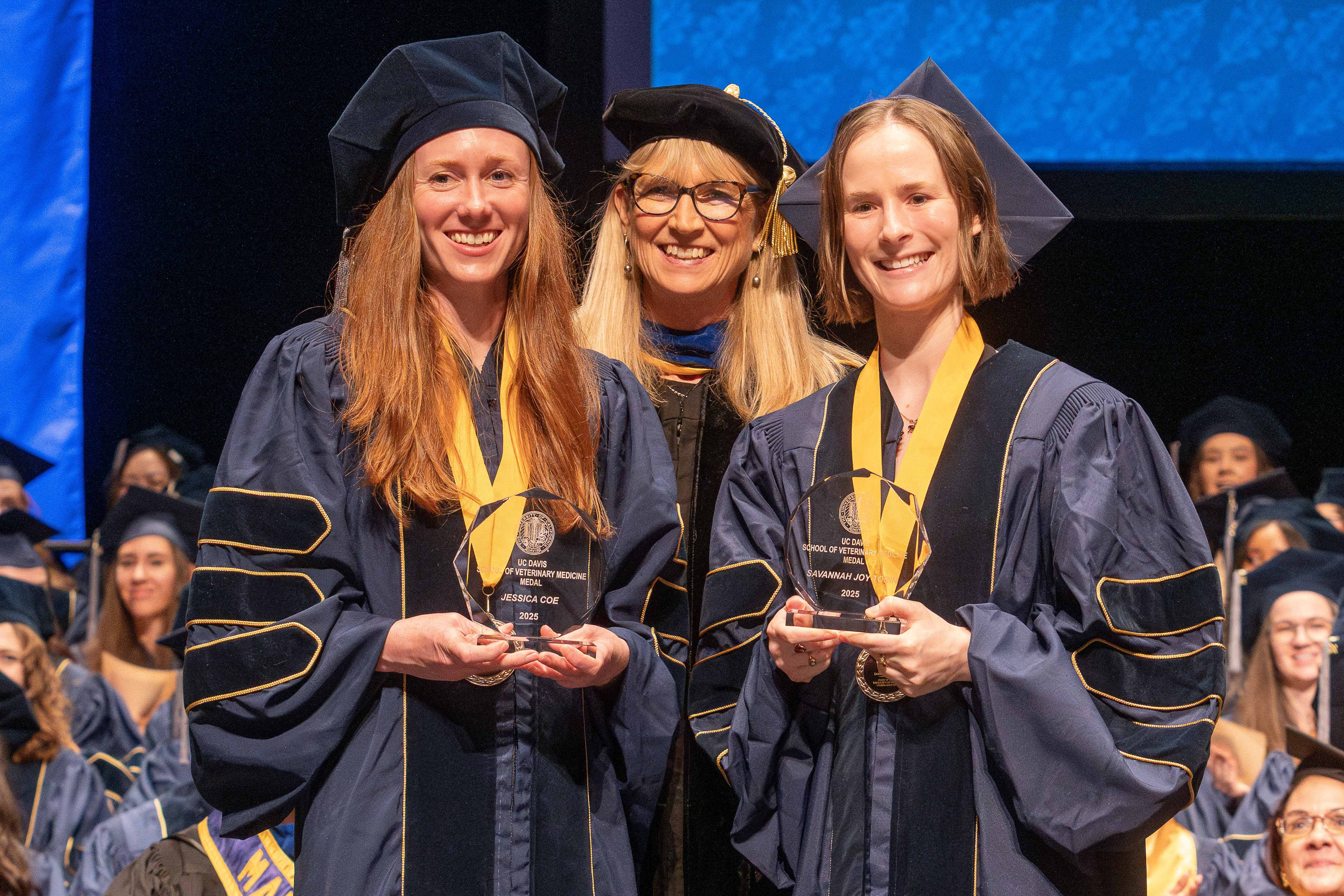 graduation ceremony with faculty member presenting awards to two students